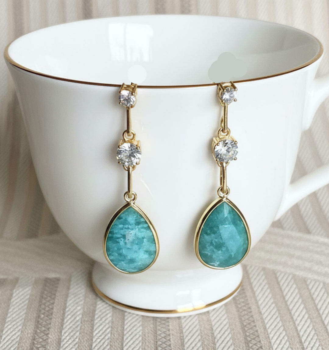 A pair of 925 sterling silver gold-tone earrings featuring amazonite gemstones and cubic zirconia, displayed against a patterned background.