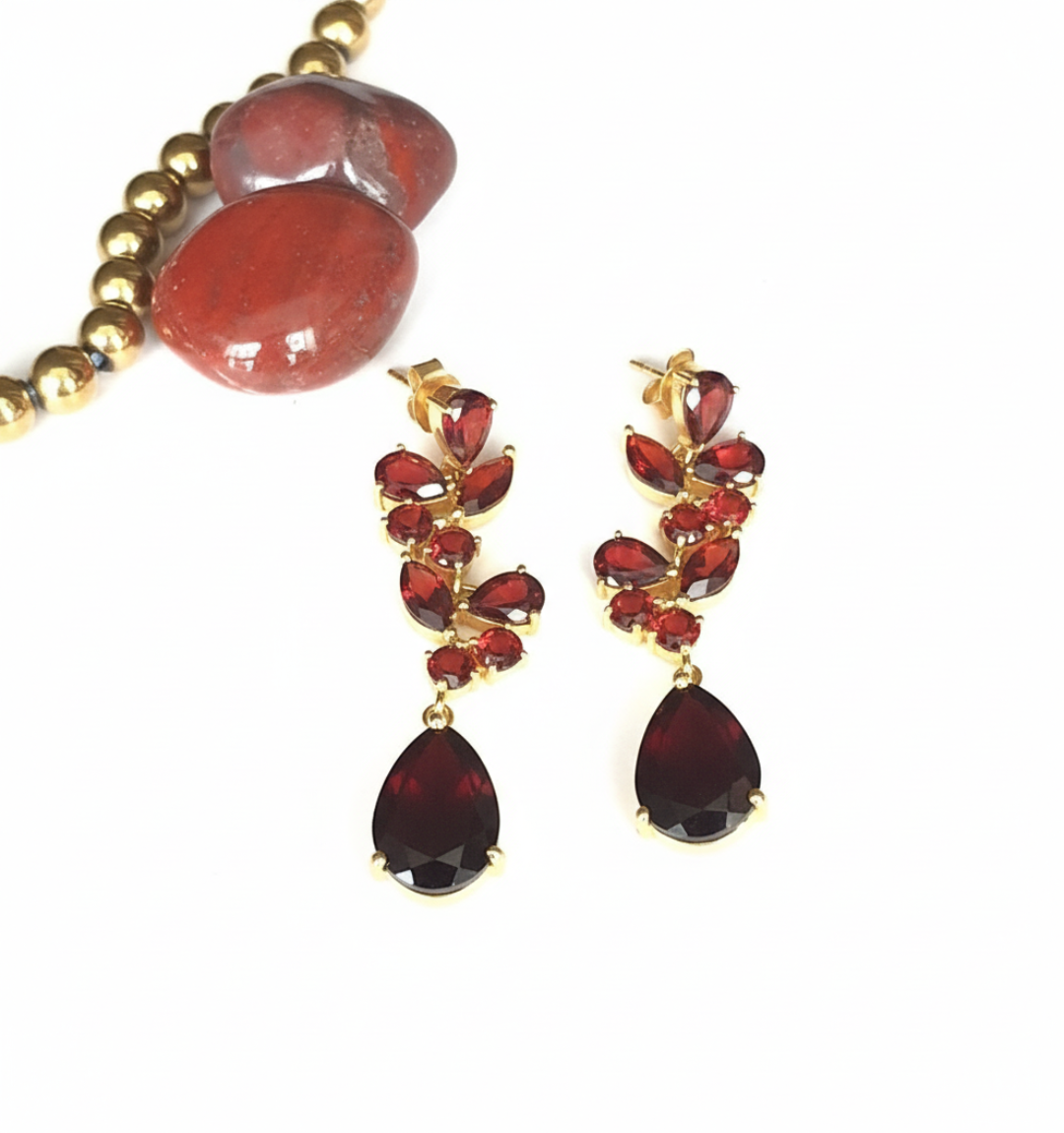 A pair of 925 sterling silver gold-plated earrings with embedded garnet stones, displayed alongside a red agate bead.