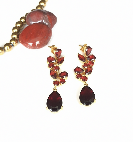 A pair of 925 sterling silver gold-plated earrings with embedded garnet stones, displayed alongside a red agate bead.