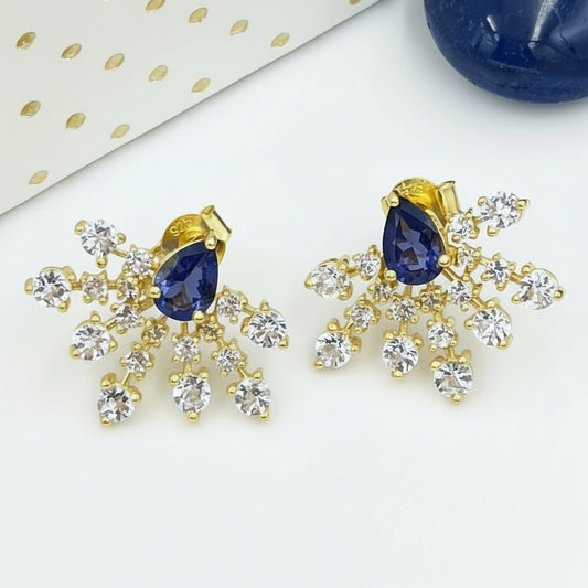 A pair of radiant cut earrings designed to mimic sunrays, featuring iolite white topaz gemstones and a yellow gold finish.