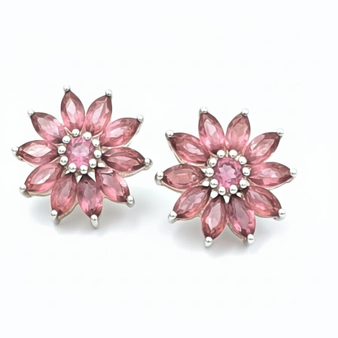 A pair of pink gemstone earrings shaped like Lotus flowers, set in silver mounting, displayed against a floral background.