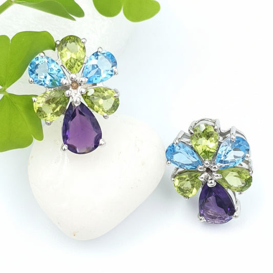 A pair of 925 sterling silver with rhoearrings designed to resemble a peacock's feathered train, made with blue topaz, peridot, and amethyst stones, displayed on a white rock.