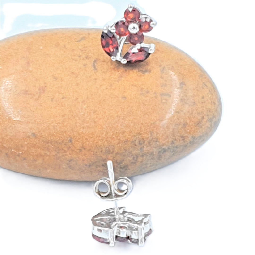 Close-up of rhodium-finished 92.5 sterling silver earrings with deep red garnet gemstones, highlighting the detailed floral styling.