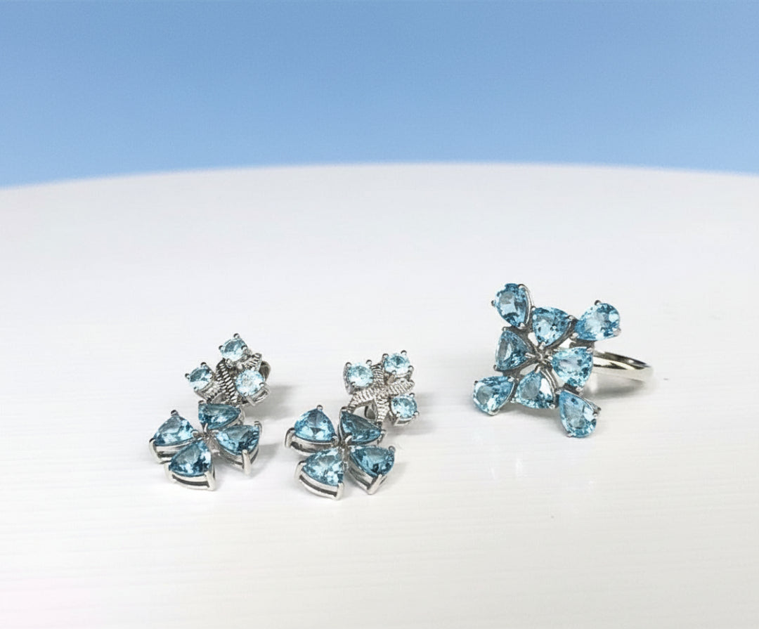 A set of 925 sterling silver jewellery set in  blue topaz earrings and a matching ring, with a silver rhodium finish, displayed against a white background.