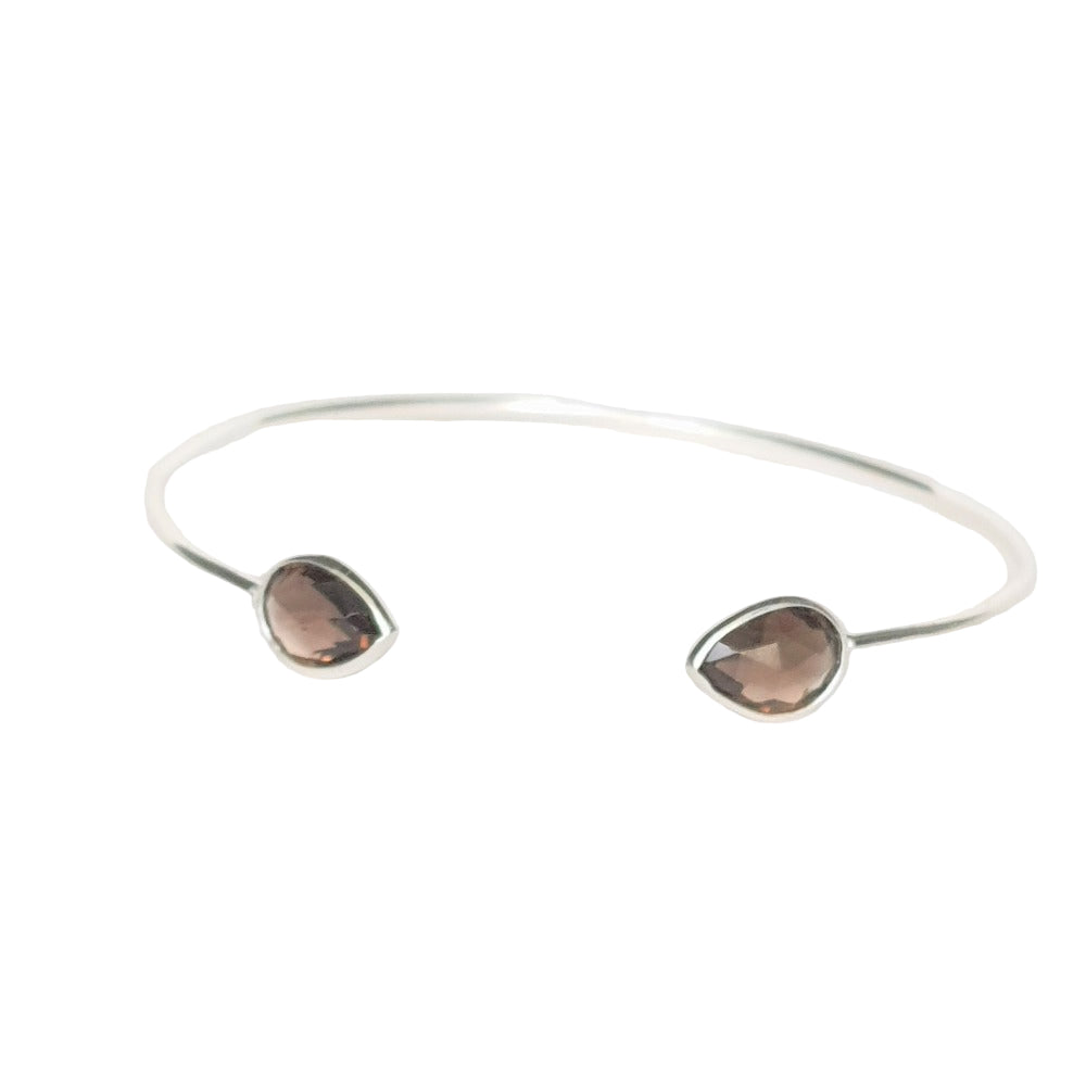 A sterling silver cuff bracelet with two smoky topaz stones set in it, on a white background.