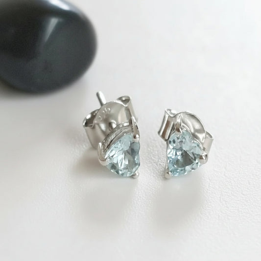 A pair of sterling silver earrings with round Aquamarine stones, displayed against a fabric background.