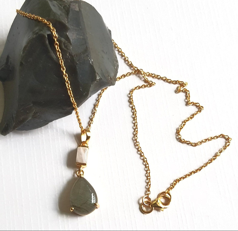 A 925 sterling silver gold-plated necklace featuring a chain link, with a pendant that includes a faceted Labradorite and a Rainbow Moonstone, displayed against a white background with a dark rock background.